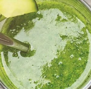 Un bicchiere di smoothie verde vivo, accanto a ingredienti freschi come spinaci e mela, su uno sfondo naturale e luminoso.