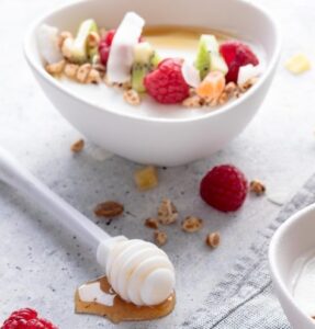 ciotola di yogurt greco con frutti di bosco colorati, miele che cola, su uno sfondo luminoso e naturale